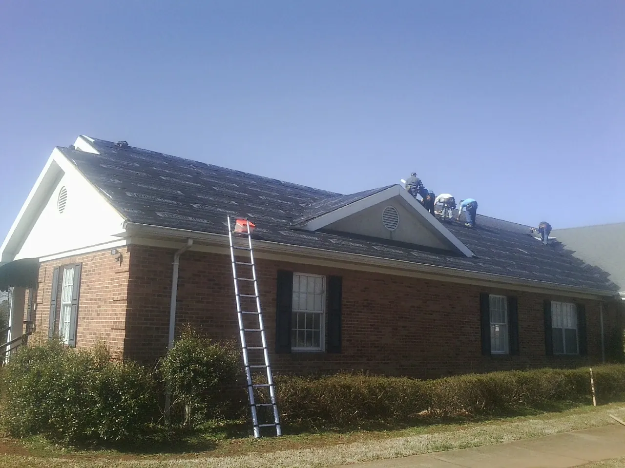 Crew tearing shingles off a brick ranch roof with a ladder set — Emergency Roof Repair work by our crew in Parksville