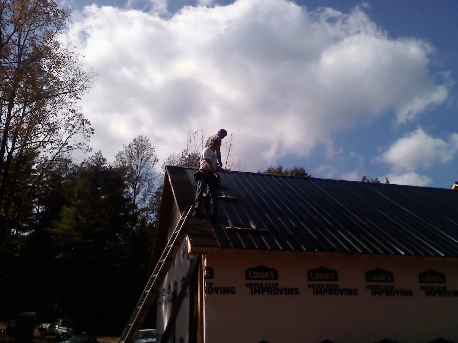 Roofer fastening dark metal panels high against a cloudy sky, from a Roof Inspection job in Parksville