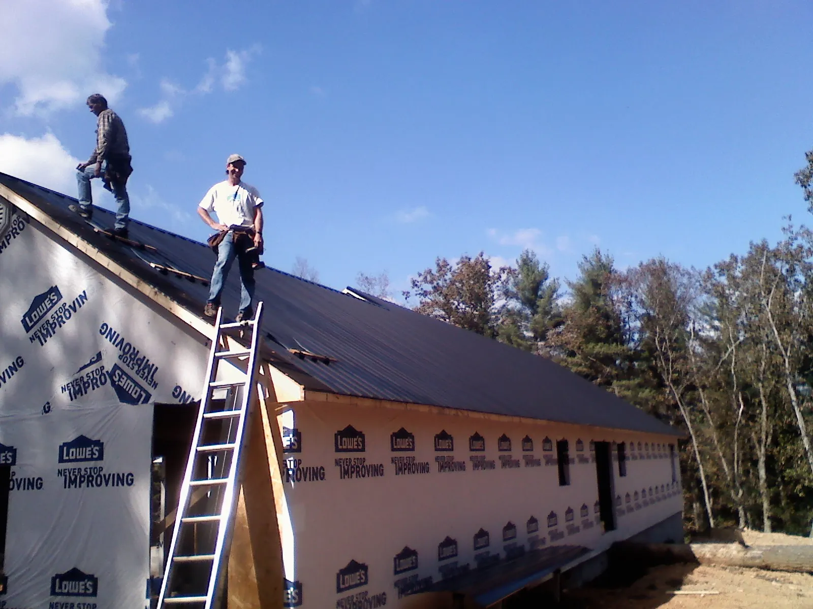Two roofers standing on a long dark metal roof over a wrapped building in Parksville